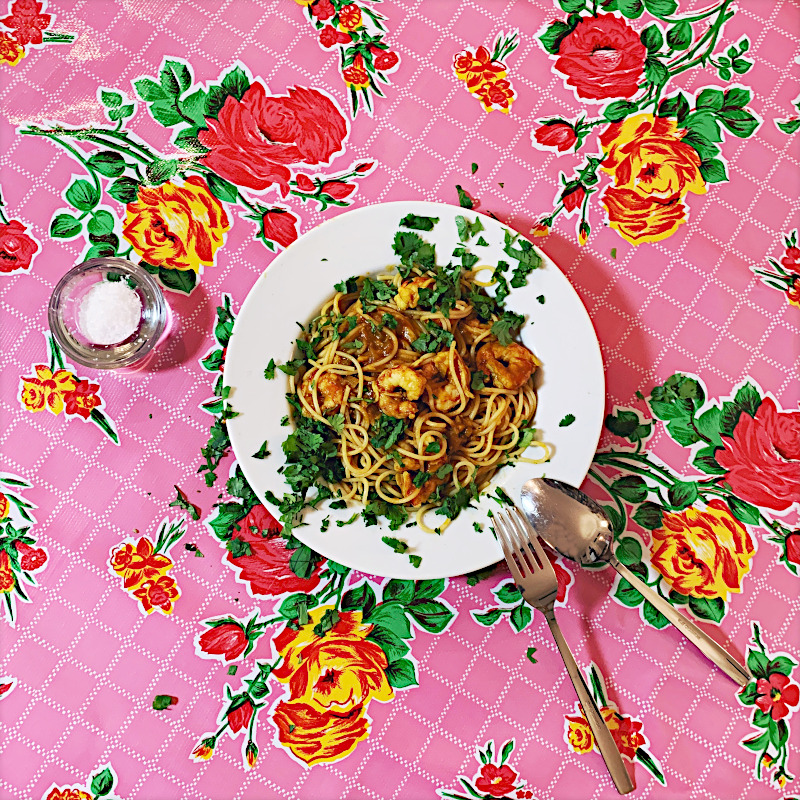 Teller Curry-Spaghetti auf ros Tischdecke mit buntem Blumenmuster
