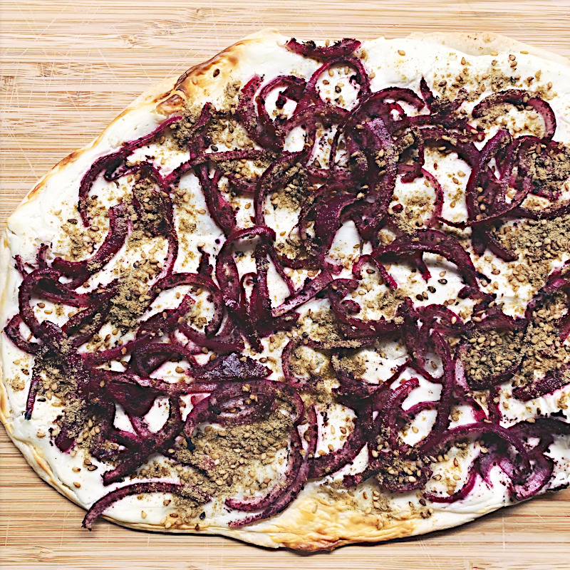 Flammkuchen gebacken mit Dukkah und Zwiebeln auf Holzbrett