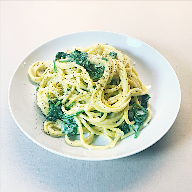 Weißer Teller auf weißem Hintergrund mit cremiger Spaghetti und Spinat