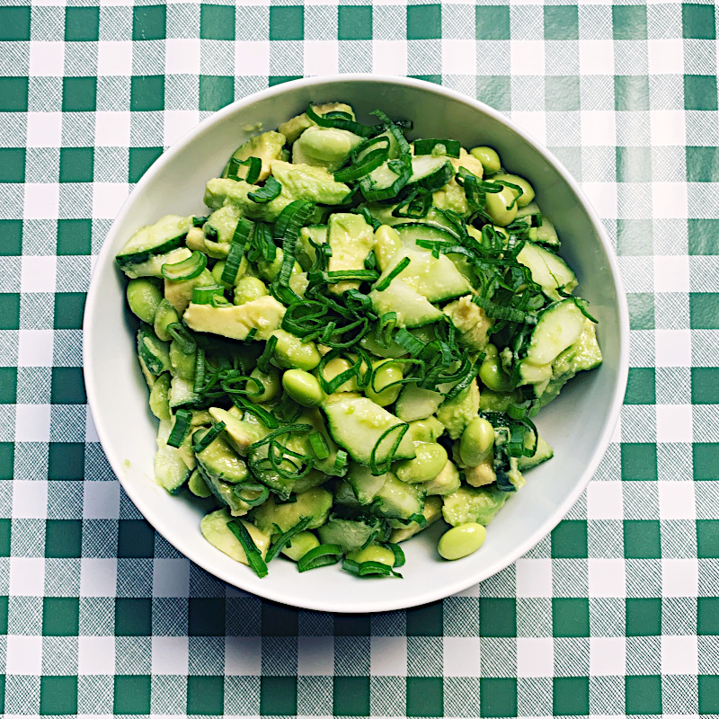 Weiße Schüssel mit grünem Avocado-Gurken-Salat auf grün-karierter Tischdecke