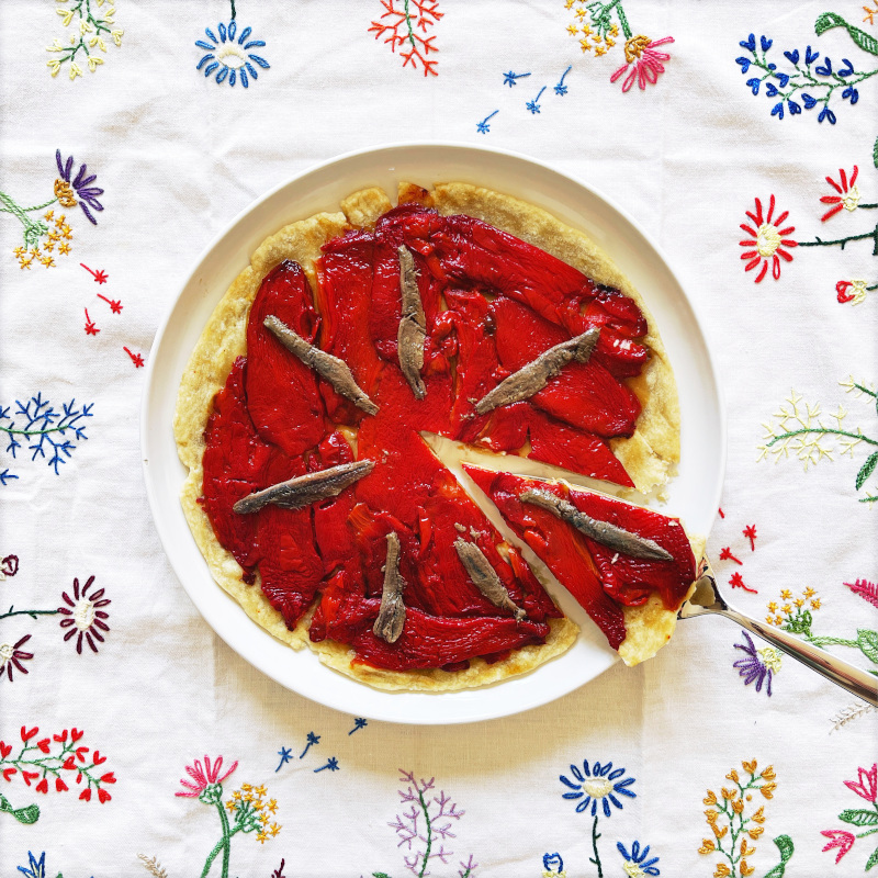 Herzhafte Paprika-Tarte mit Sardellen auf weißer Platte auf frühlingshafter Tischdecke