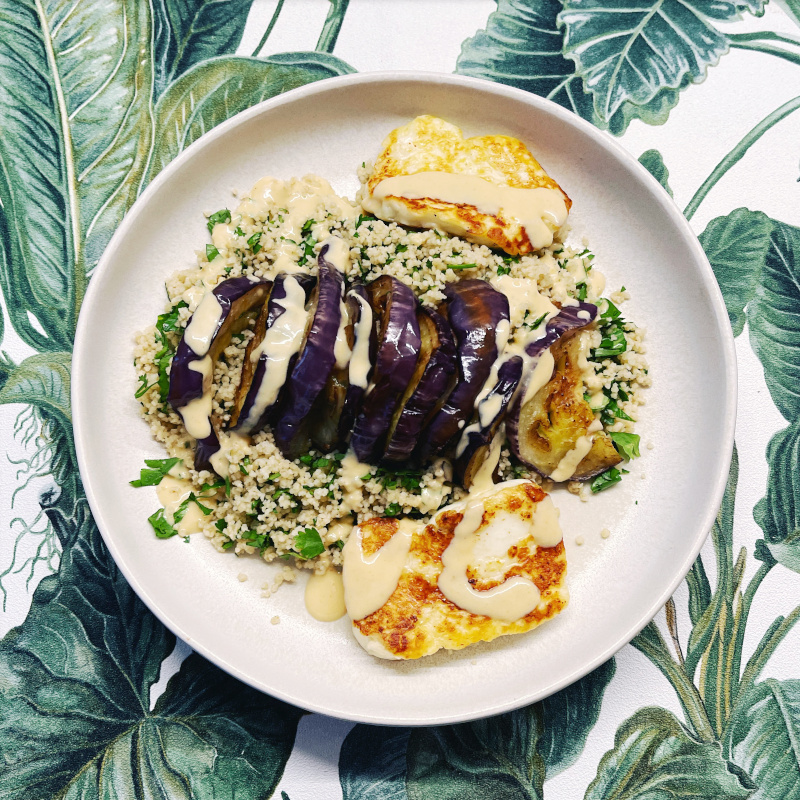 Teller mit Couscous-Auberginen-Salat mit Amba-Tahini-Dressing auf bunter Tischdecke