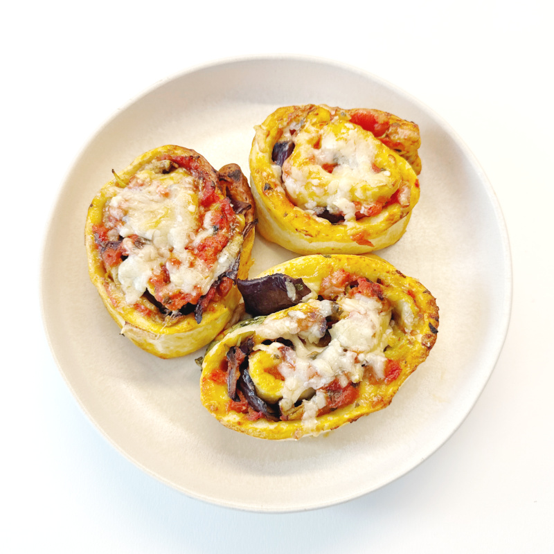 Schnelle Parmigiana Pizza-Schnecken mit Aubergine auf weißem Teller.