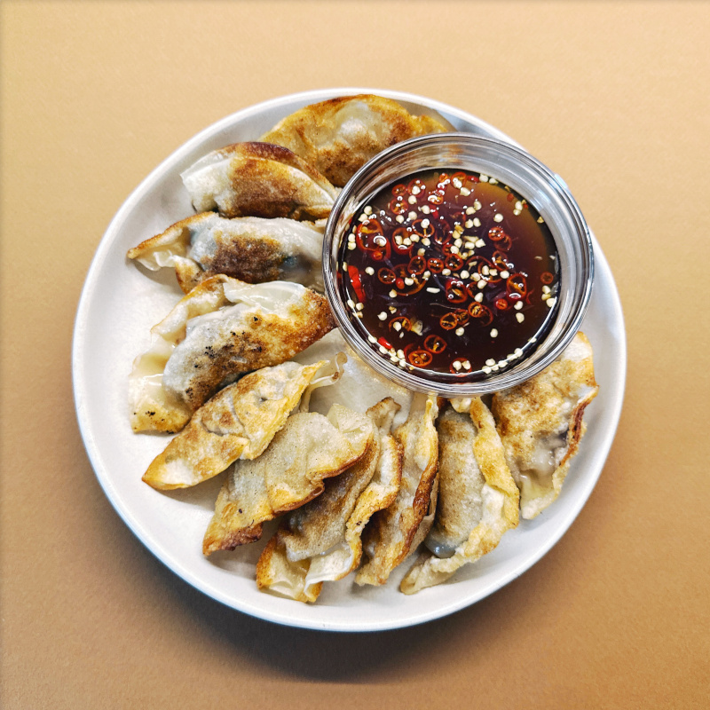 Gebratene Gyoza auf einem weißen Teller mit einer Schale mit scharfem Dip