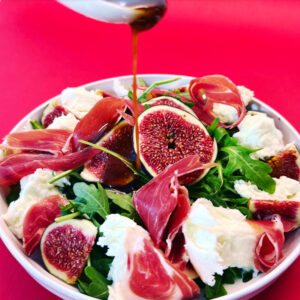 Ruccolasalat mit Feigen und Mozzarella in weißem Teller auf rotem Untergrund