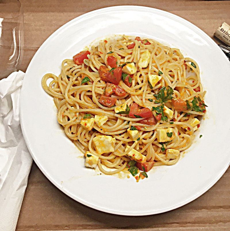 Teller mit Sommer-Spaghetti, Tomaten und Mozzarella auf Holztisch