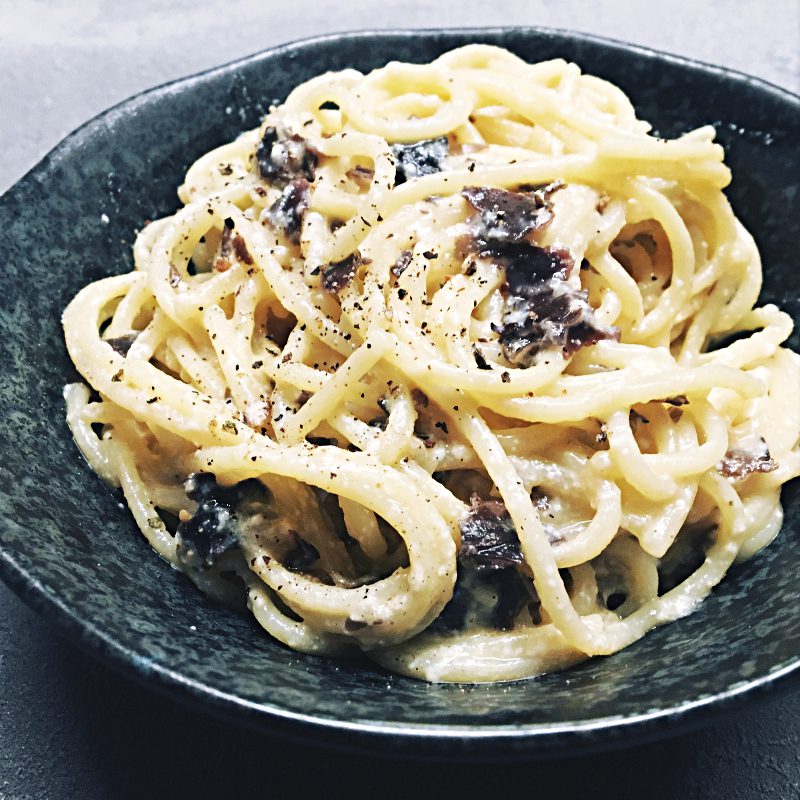 Vegane Spaghetti Carbonara-Style in dunkler Schale serviert