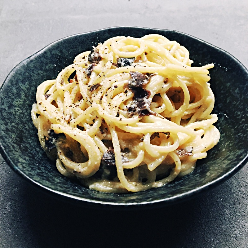 Vegane Spaghetti Carbonara-Style in dunkler Schale auf schwarzem Hintergrund