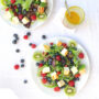Zwei Teller Salat mit bunten Beeren und Curry-Dressing im Glas