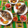 Teller mit gebratenen Fischen, Kochbananen und scharfer Piri-Piri-Sauce auf bunter afrikanischer Tischdecke