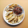 Gebratene Gyoza auf einem weißen Teller mit einer Schale mit scharfem Dip